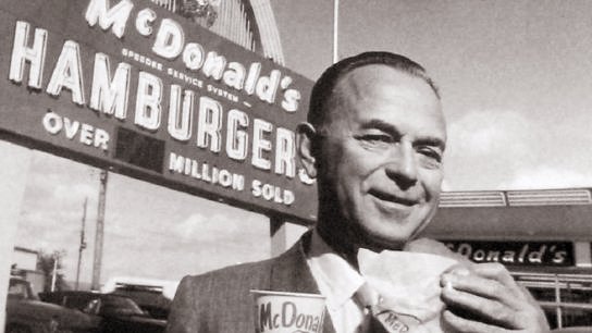 Ray Kroc, el fundador de McDonald's, sonriendo mientras sostiene una hamburguesa en su mano