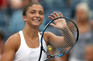 Sara Errani ejecutando un golpe de derecha en una pista de tierra batida, vestida con ropa deportiva italiana, con las gradas desenfocadas al fondo.